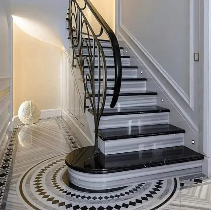 Curved staircase with black marble treads on grey striped risers, a wrought-iron railing and a circular mosaic floor at the base