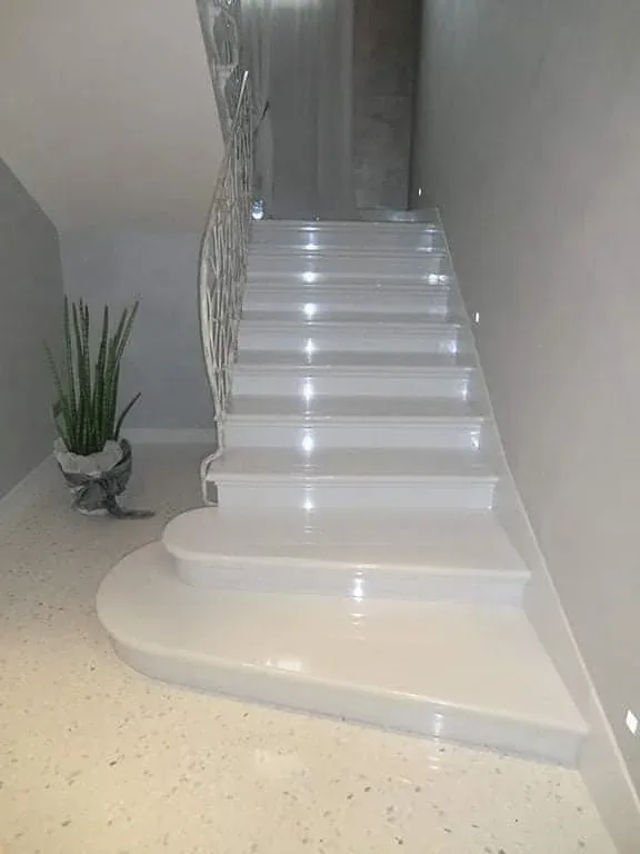 Polished white marble staircase with rounded bottom steps, a wrought-iron railing and recessed step lights