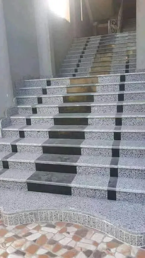 Wide staircase in speckled grey granite with a black inlay strip up the centre and a curved bottom step edged in mosaic
