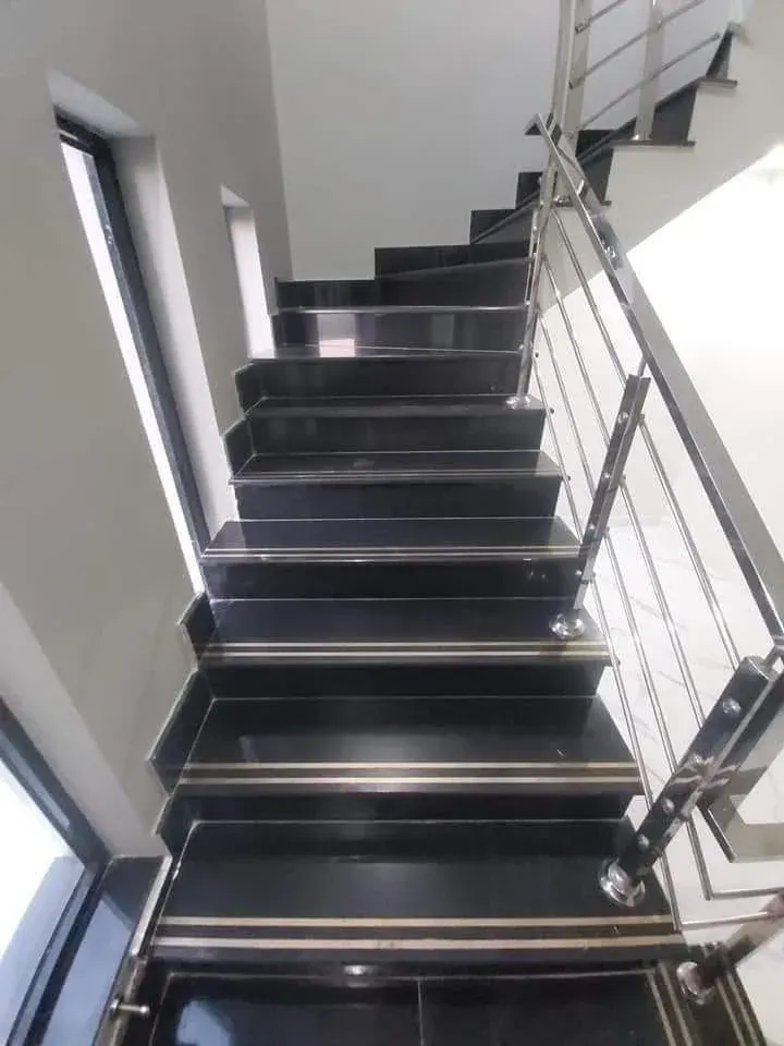 Black granite staircase with two brass anti-slip strips on every tread and a stainless steel railing