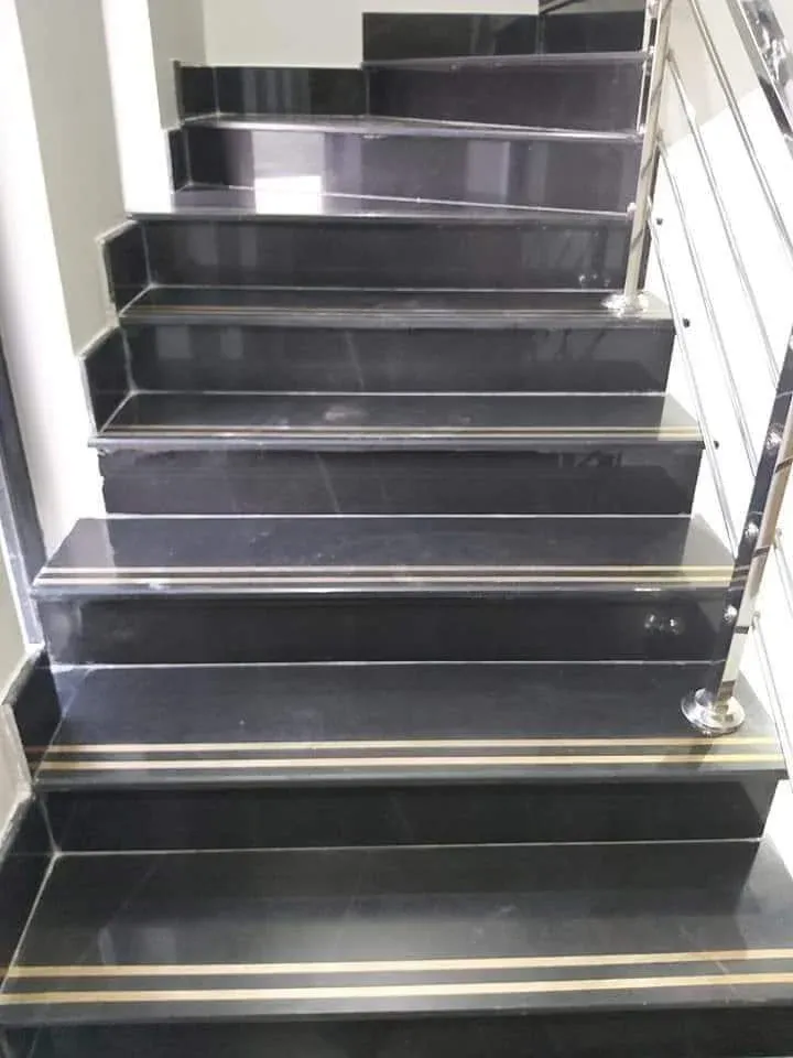 Black marble staircase with brass nosing strips on each tread, turning at the top, with a stainless steel railing