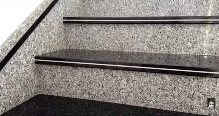 Close-up of black granite stair treads with a steel inlay line, above speckled grey granite risers
