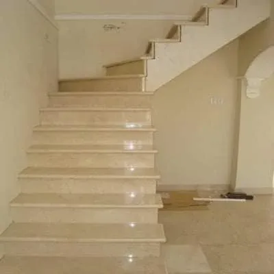 Cream marble staircase with polished treads and risers, turning at the top beside an arched opening